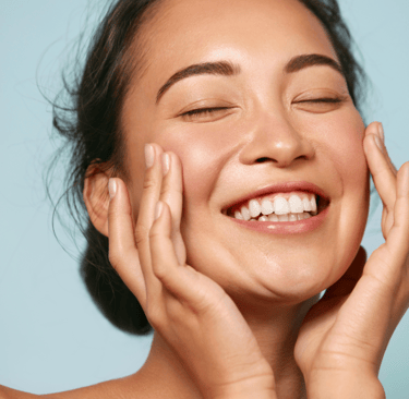 Smiling woman with clear, healthy skin touching her face, representing smooth skin