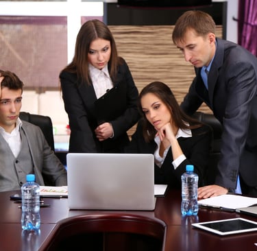 Stressed business team analyzing data on a laptop during a corporate office meeting.