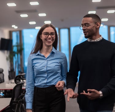 Two diverse young professionals walking and talking in a modern, open-plan office setting.