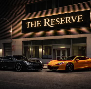 Black Porsche and orange McLaren luxury sports cars parked outside The Reserve building at night.