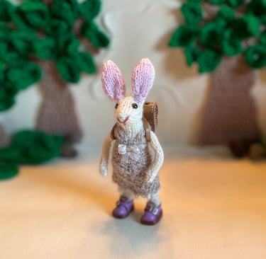 a small knitted bunny ornament wearing a crochet dress and handmade leather shoes and satchel