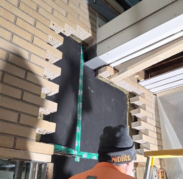 A construction worker installing black building insulation and flashing into an exterior brick wall.