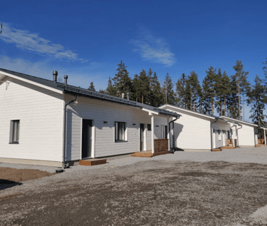 Modern white wooden row houses with gravel driveways under a clear blue sky and pine trees.