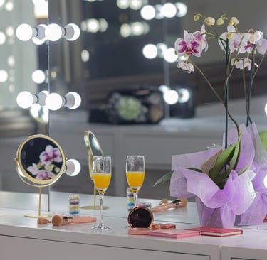 Tocador de lujo con espejo Hollywood iluminado, mimosas, pinceles de maquillaje y orquídea violeta.