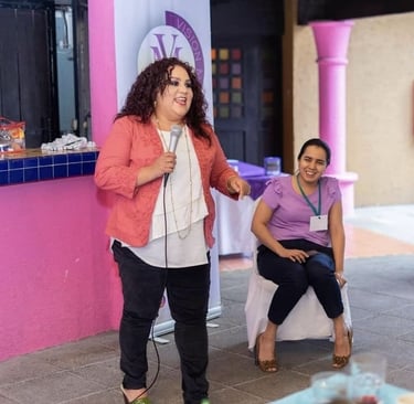Una oradora sonriente con cabello rizado sosteniendo un micrófono y dando una presentación en vivo