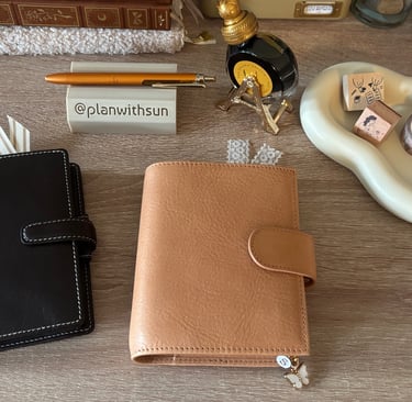 An apricot Moterm pocket planner and a tan Filofax planner on a desk with fountain pens and stamps.