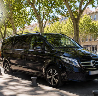 Luxury black Mercedes van for Marseille cruise excursions parked on a tree-lined street near a fountain.