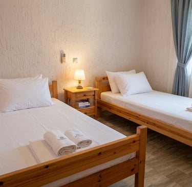Two single wooden beds with white linens and a nightstand in a bright hotel room.