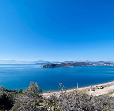 Aerial view of a scenic blue bay and sandy beach in Greece with mountains under a clear sky.