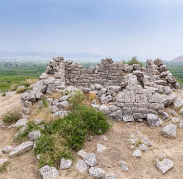 Ancient stone ruins of the Pyramid of Hellinikon overlooking a lush Greek valley landscape.