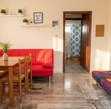 Modern studio apartment featuring a red sofa, wooden dining set, and colorful patterns.