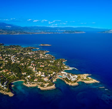 Aerial view of a coastal Greek town with luxury villas and turquoise Mediterranean sea water.
