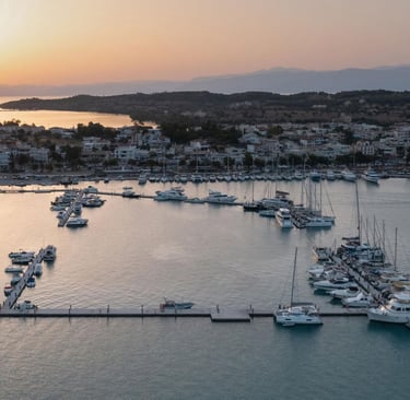 Aerial sunset view of luxury yachts and sailboats docked in a Mediterranean coastal town marina.