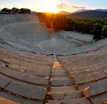 Golden sunset over the ancient Theater of Epidaurus in Greece with stone seating and mountains.