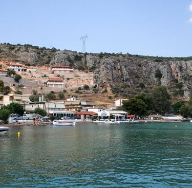 Scenic coastal village in Greece with waterfront tavernas and boats on turquoise sea water.