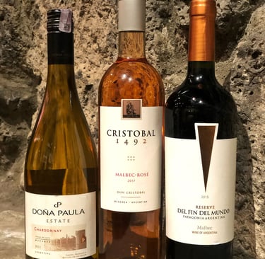 Three bottles of Argentine wine, including Chardonnay, Malbec Rosé, and red Malbec, against a stone wall.