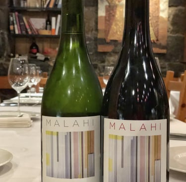 Two bottles of Malahi Armenian wine on a restaurant table with wine glasses and a bookshelf background.