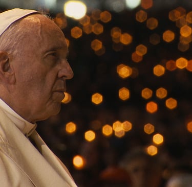 Pope Francis in profile at night with golden bokeh candle lights in the background.