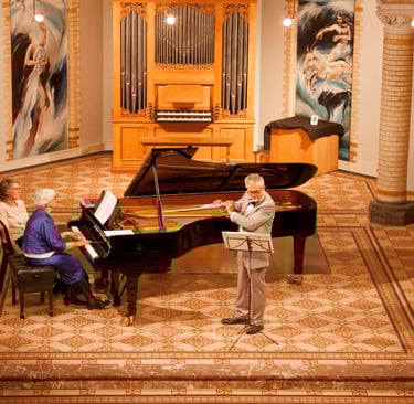 Classical music concert featuring a flutist and pianist performing together in a chapel with a pipe organ.