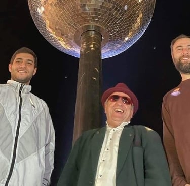 Three men smiling beneath the Sunsphere tower at night in Knoxville World's Fair Park.