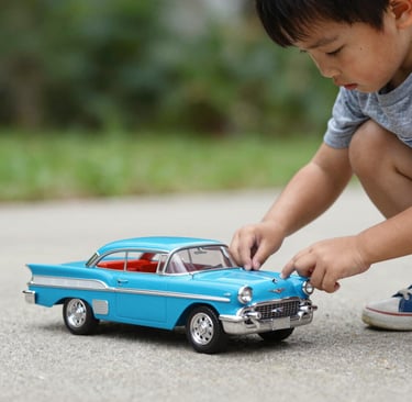 A young boy playing with a classic blue vintage model toy car on a paved sidewalk outdoors.
