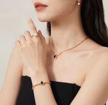 Woman wearing a gold jewelry set with a pearl ring, black stone pendant necklace, and matching bracelet.