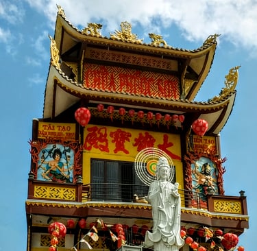 Exterior view of a vibrant yellow pagoda in Soc Trang, Vietnam with a white Guan Yin statue.