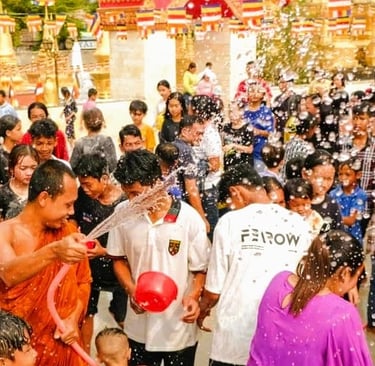 A monk in orange robes sprays a hose at a crowd of smiling people during a water fight at a Khmer pa