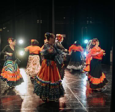 Traditional flamenco dancers performing in colorful ruffled skirts on a theater stage with stage lights.