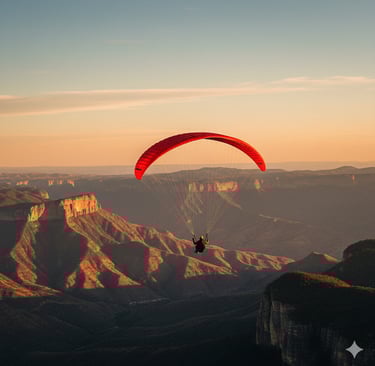 A person paragliding with a red wing over mountain canyons during a golden sunset.
