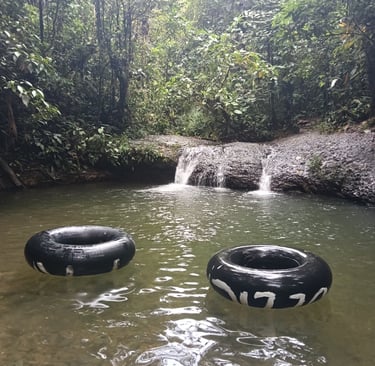 Black inner tubes floating in a tropical river pool near a small jungle waterfall.