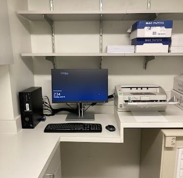 Office workstation with a desktop computer, monitor, keyboard, and printer on a white desk with shelves.