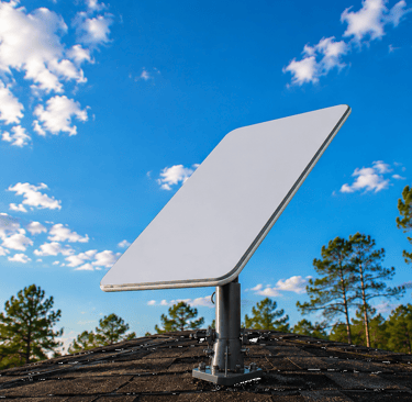 A Starlink satellite internet dish mounted on a residential roof under a clear blue sky with pine trees.