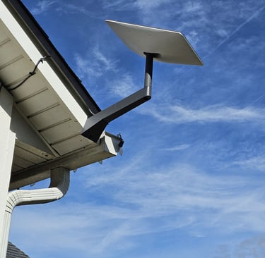 A Gen3 Starlink satellite internet dish mounted on a residential roof eave against a blue sky.