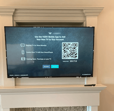 Above-fireplace mounted VIZIO smart TV displaying a setup screen with a QR code for the mobile app.