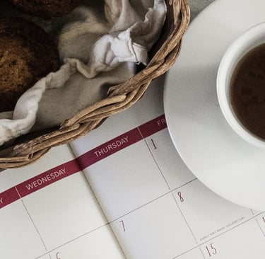 Calendar with cup of coffee and muffins on white table