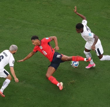 Jude Bellingham in an England kit dribbles past two defenders on a green soccer pitch during a match.