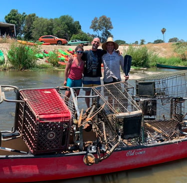 Group standing beside a kayak filled with trash and debris collected during a river cleanup.