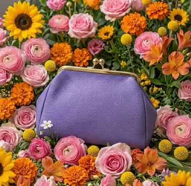 Purple leather clutch purse with a gold kiss-lock clasp nestled in a vibrant bouquet of pink roses and sunflowers.