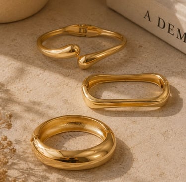 Gold statement bracelets styled on a beige surface with warm sunlight and neutral decor.