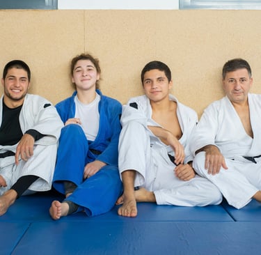 Group of Brazilian Jiu Jitsu participants sitting on the ground smiling