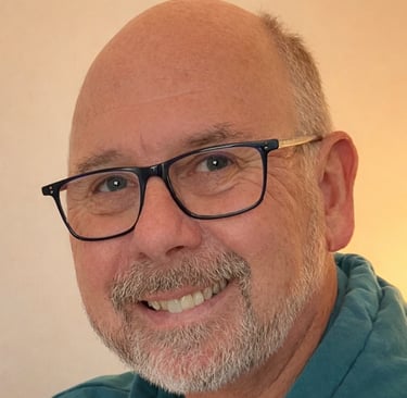 Smiling bald man with glasses and a grey beard wearing a blue shirt.