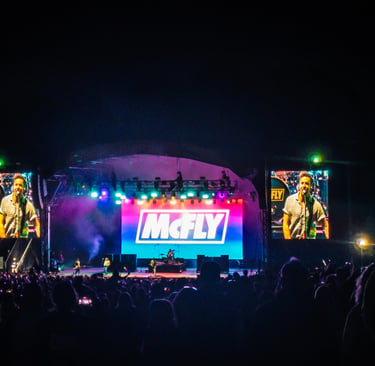 British pop rock band McFly performing live on a brightly lit concert stage for a large crowd at night.