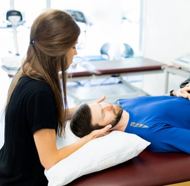 A female physical therapist providing neck manual therapy to a male patient in a clinic.