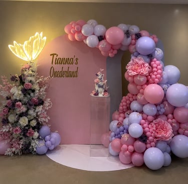 Elegant pink and purple 'Tianna's Onederland' first birthday party decoration with balloon arch, floral arrangements, and a