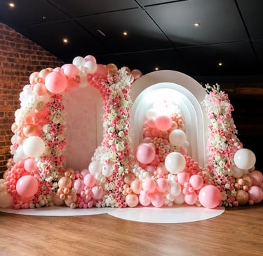 Elegant pink and white balloon arch with floral arrangements for a luxury event backdrop.