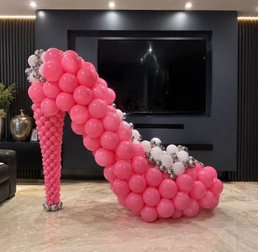 Giant pink and silver balloon high heel sculpture, a decorative party centerpiece in a modern living room.