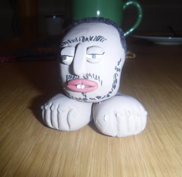 Handmade clay sculpture of a bearded man's head sitting on two large feet on a wooden table.