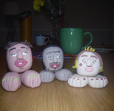 Three unique handmade clay figurines with expressive faces and large feet displayed on a wooden table.