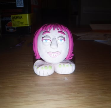 Handmade clay sculpture of a character head with pink hair and two large feet.